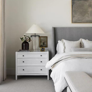 A gray bedframe with white bedding and a white nightstand.