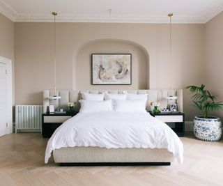 large bedroom with arch behind bed, pale wooden flooring, netural wall colour and white bedding