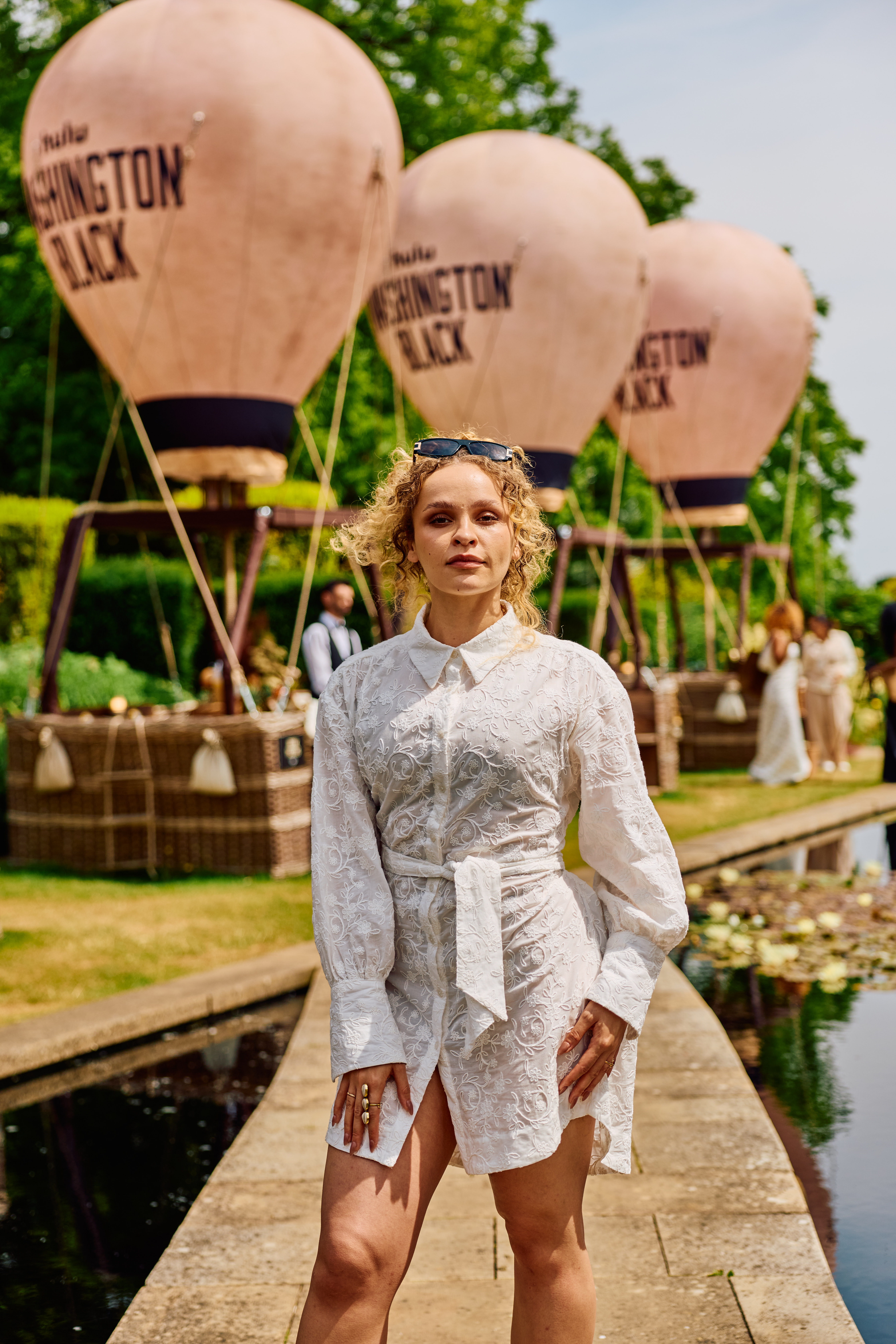 Iola Evans, posing in front of miniature hot air balloons reading 'Washington Black' in a poolside garden.