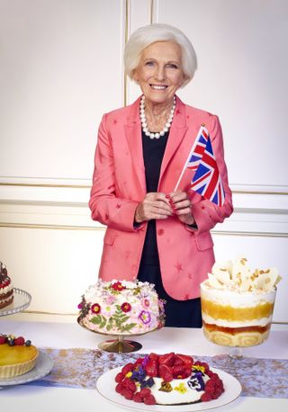 Dame Mary Berry holding a Union Jack flag surrounded by cakes.
