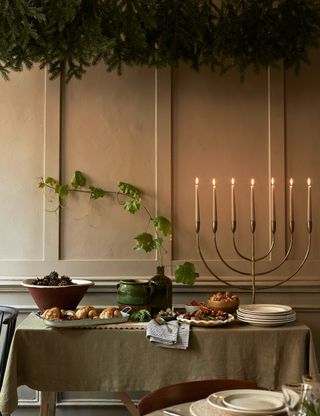 A side table with roast poussin and dishes for dinner against a wood panelled wall and lit candles in a menorah