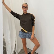 Iris Law poses for a photo wearing a brown v-neck knit with ruffle shoes and black curved-heel wedges.