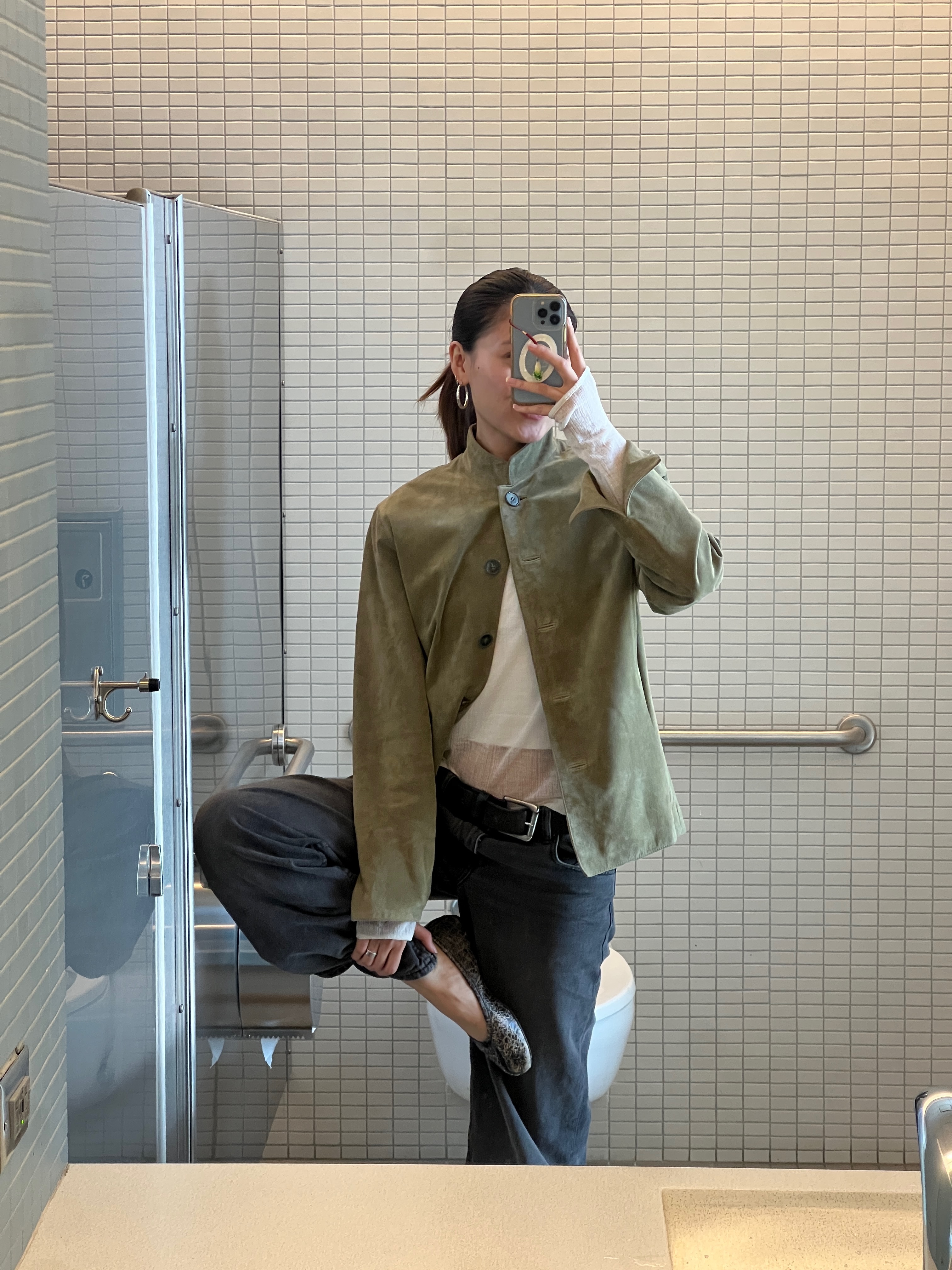 Vivan Li in a grey jacket, white sheer top, black pants, and flats in a mirror selfie