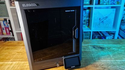 Elegoo Centauri Carbon printer on a wooden table in front of board game shelves