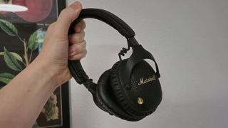 The Marshall Monitor III ANC headphones being held up in front of a wall