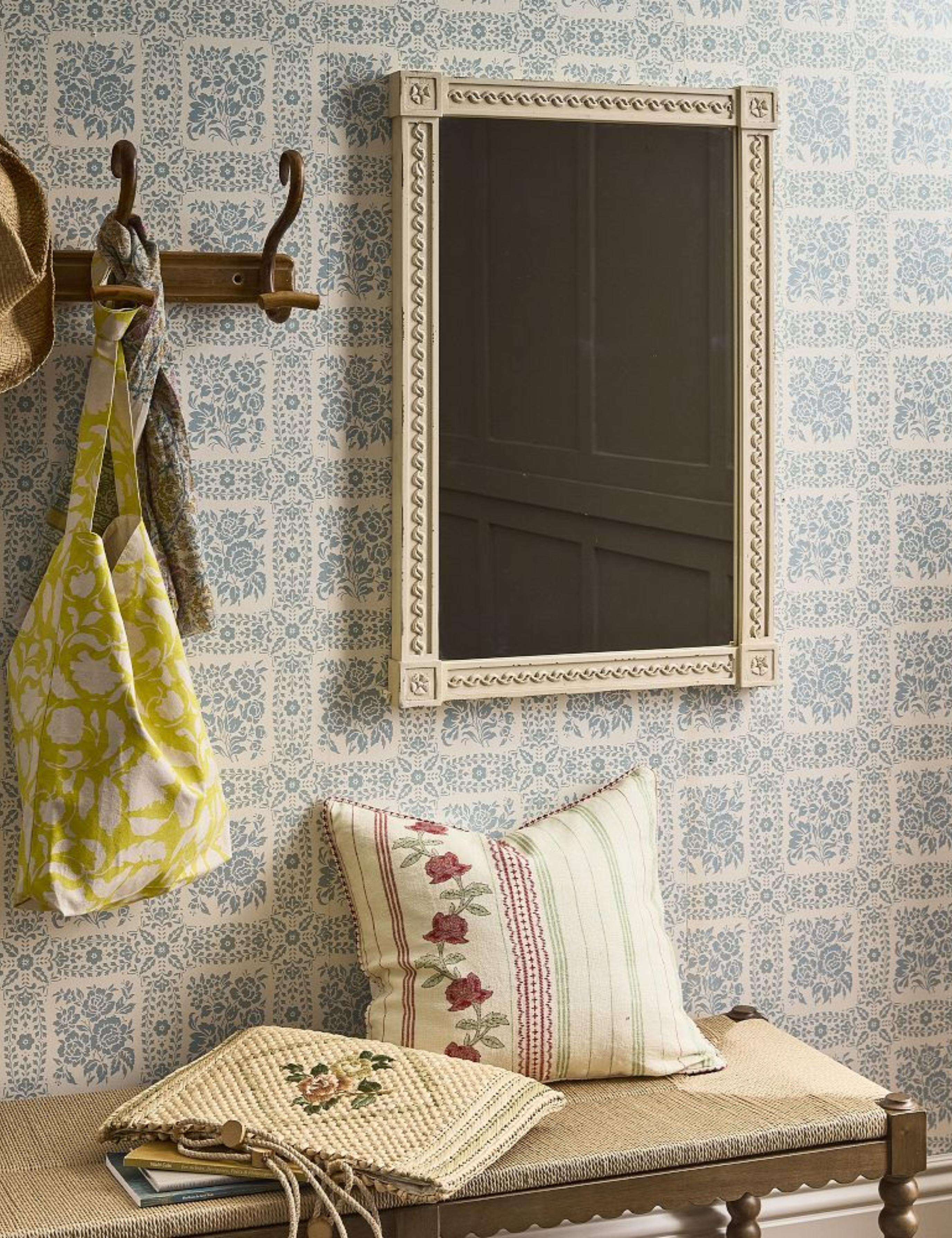 Decoratively carved light sand wood frame mirror hanging in an entryway area featuring a bench and patterned wallpaper