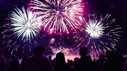 A silhouetted crowd looking up at fireworks.