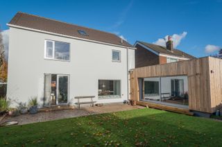 A passivhaus with a white painted exterior and a timber frame single storey extension with a green lawn