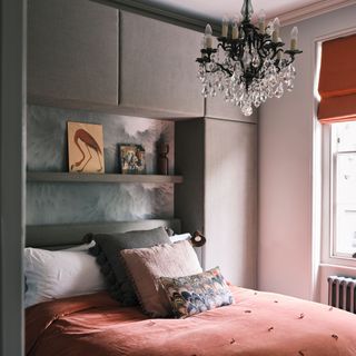 Dark pink bedding set with decorative cushions on top of bed, shelving above headboard and black chandelier