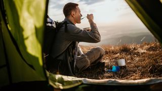 A man sits outside his tent eating a camping meal