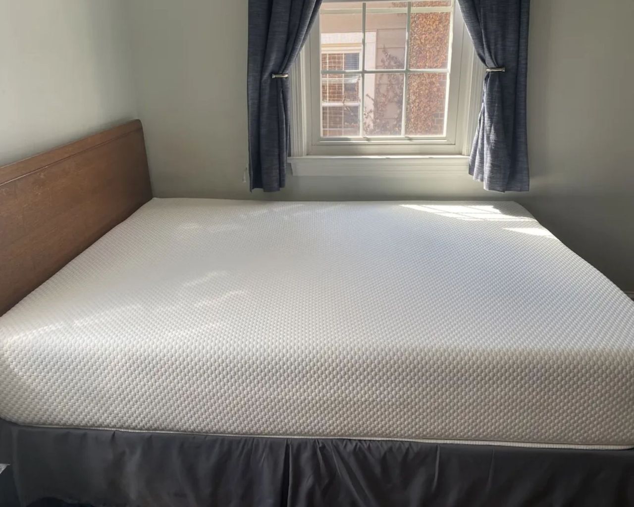 The Nolah Original Mattress in a white bedroom on a wooden bedframe with large window and navy curtains.