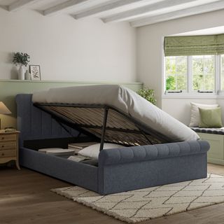 A side operating ottoman bed with grey upholstery in a green and white decorated bedroom