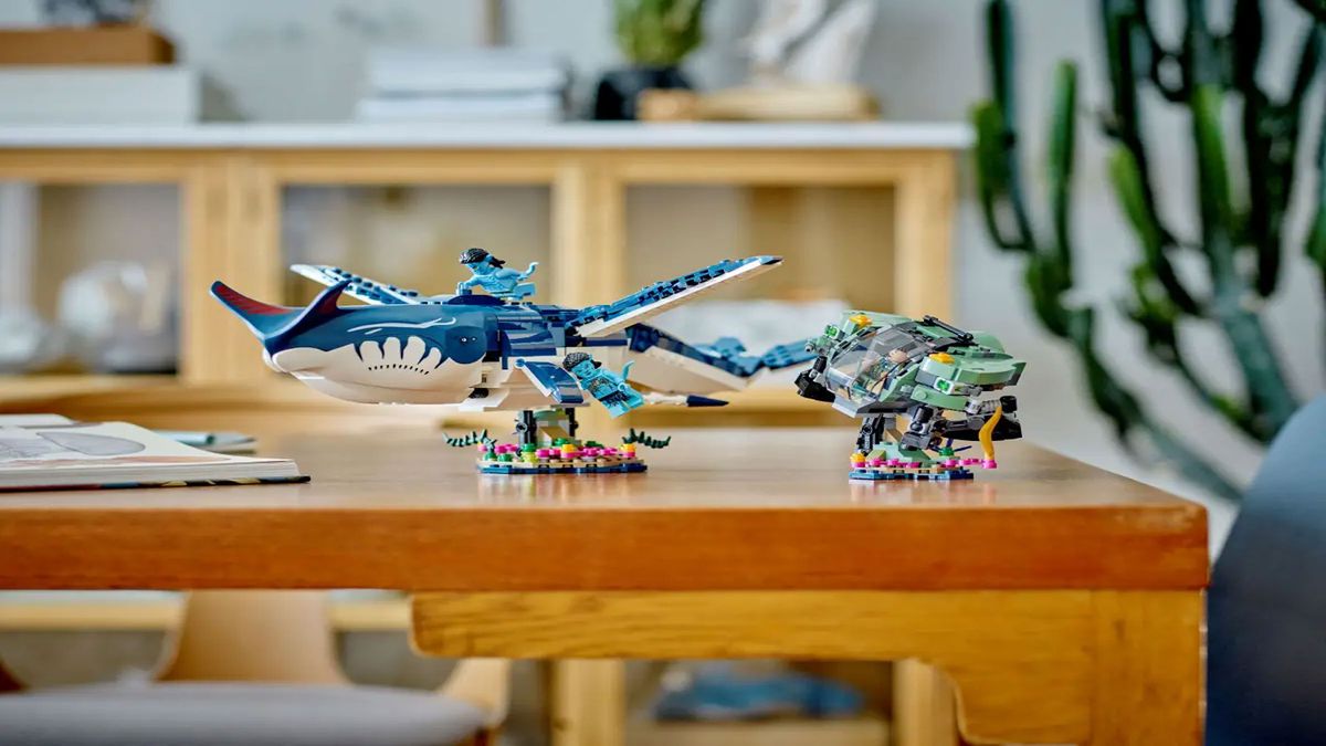 A large blue brick-built whale is displayed next to a mechanical crab and a blue minifigure, on a brown wooden table with plants in the background.