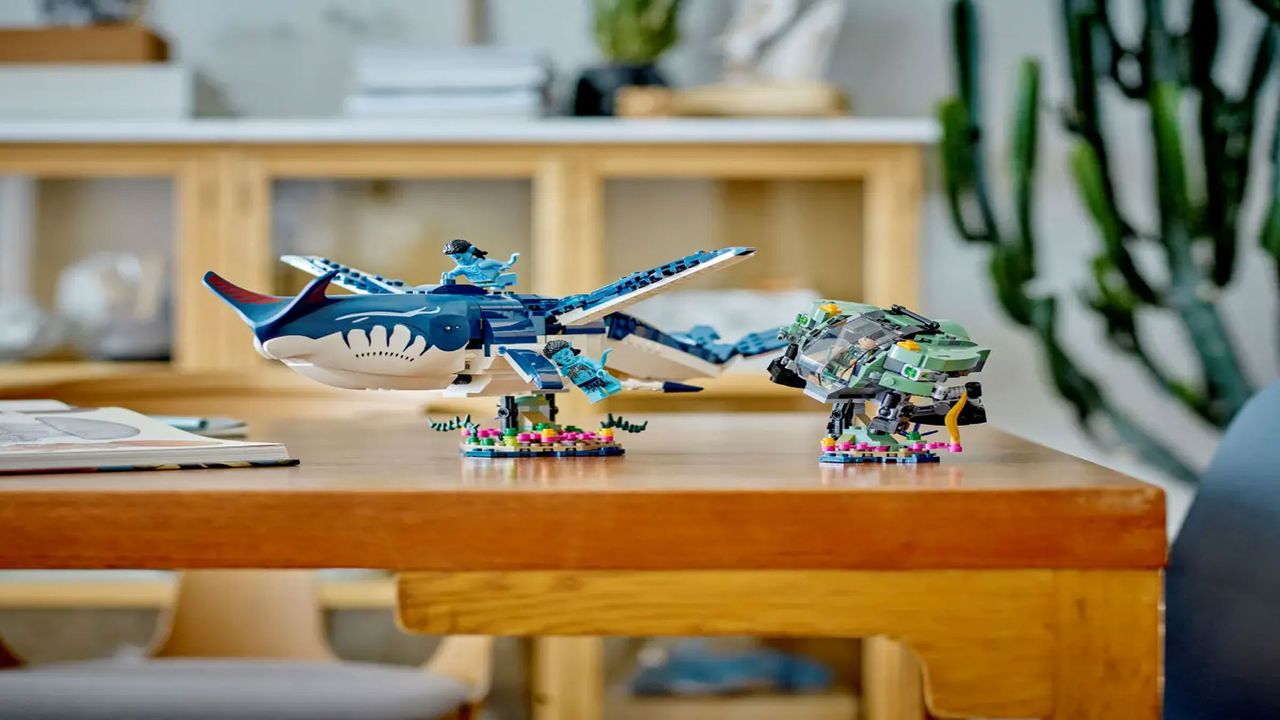A large blue brick-built whale is displayed next to a mechanical crab and a blue minifigure, on a brown wooden table with plants in the background.