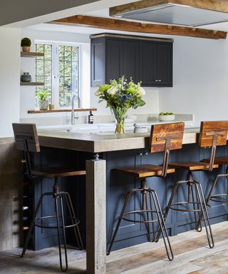 A kitchen with a blue-grey island and reclaimed wood-topped breakfast bar with leather and metal bar stools