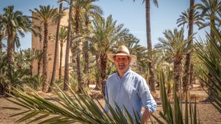Monty Don in a straw hat stands in front of palm trees in Monty Don's Spanish Gardens