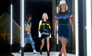 Models wear blue t-shirt with beige top and blue trousers, black and multicolour stripes dress with black and white bomber jacket, and dark blue dress with bucket hat