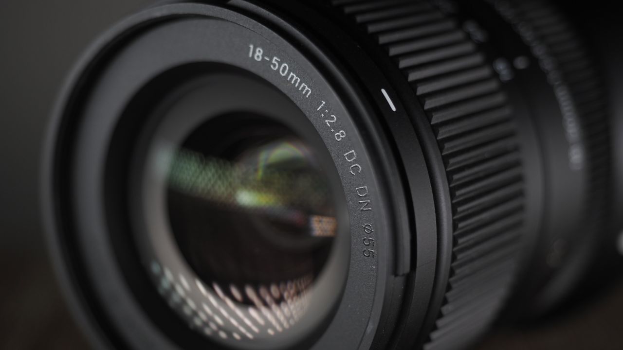 The Sigma 18-50mm f/2.8 DC DN | C Canon RF lens on a wooden surface against a dark background with moody lighting