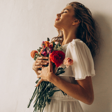 woman with glowing tan, wavy hair and white dress holding a bunch of flowers