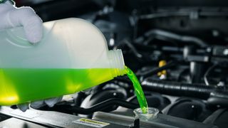 Close-up image of a transparent, unlabelled bottle of fluorescent green antifreeze being poured into a car engine