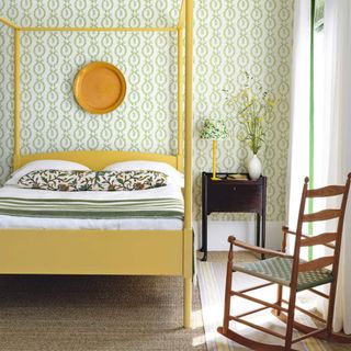Bedroom decorated with lime green and white wallpaper, a yellow 4 poster bed and wooden rocking chair.