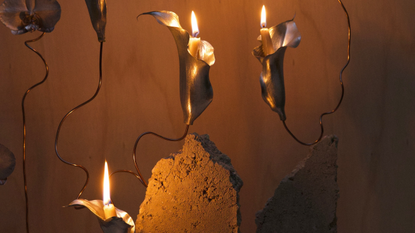 A close-up of an artistic installation with metal sculpted calla lilies with mini candles woven into concrete blocks