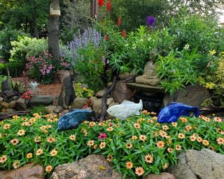 Colourful garden with green, orange, purple and red plants with fish and water feature and rockery