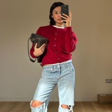 @smythsisters wears a red cardigan, light blue distressed jeans and a khaki bag