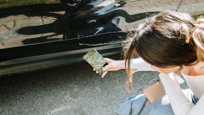 A woman uses her phone to take photos of her damaged car after an accident.