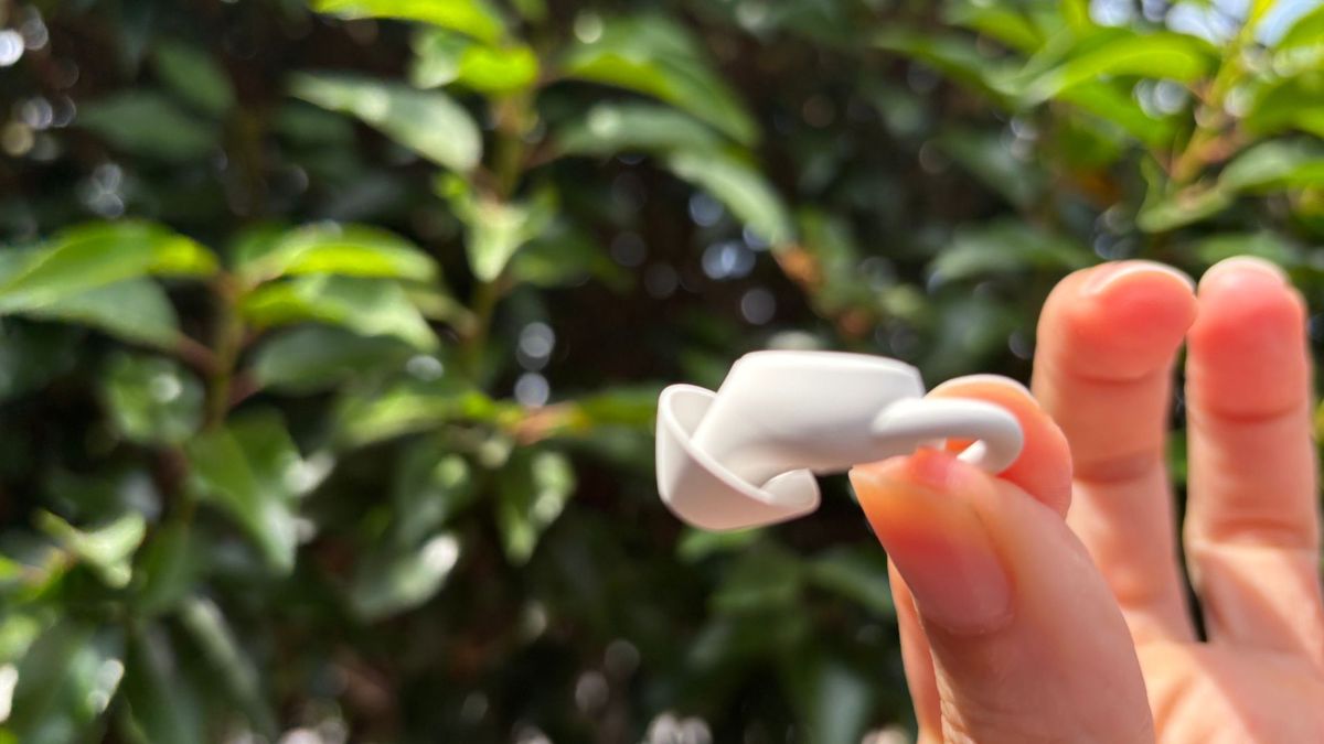 The image shows someone holding up the tiny Ozlo Sleepbud 2 between their thumb and forefinger