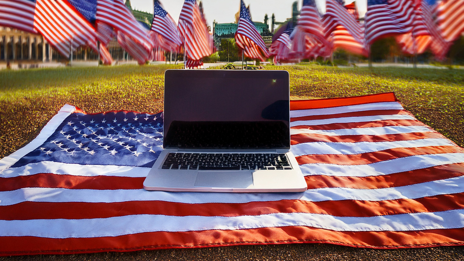 A laptop sat on a USA flag on a sunny day