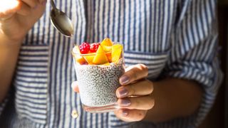 Woman holding pot of yoghurt with chia seeds and fruit on the top