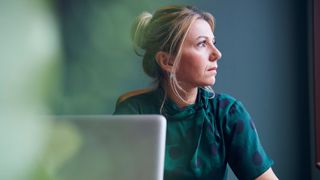 Woman looking out of the window in front of laptop screen and desk plant