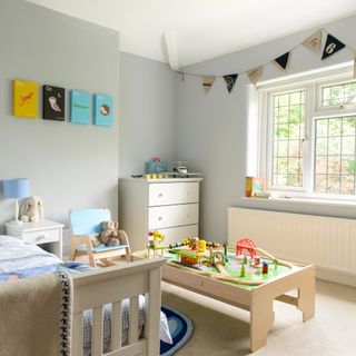 A children's room painted in light grey with white and light furniture and a large activity toy in the middle