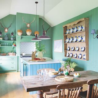 cottage kitchen with green walls and base units, blue island, open shelves and farmhouse table