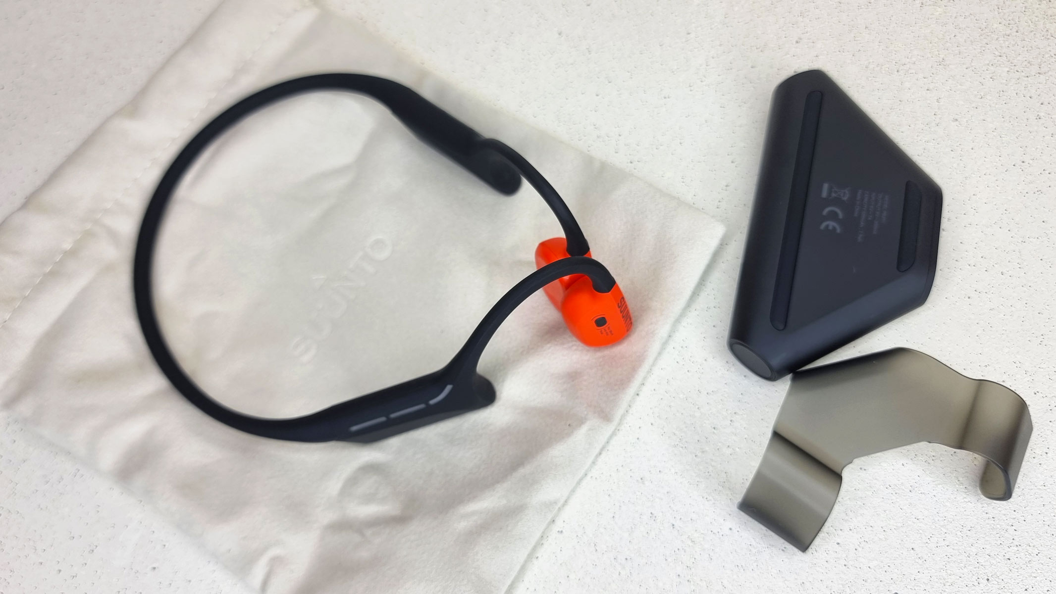 The Suunto Wing 2 bone conduction headphones, a carrying case and a power bank, all laid out on a table