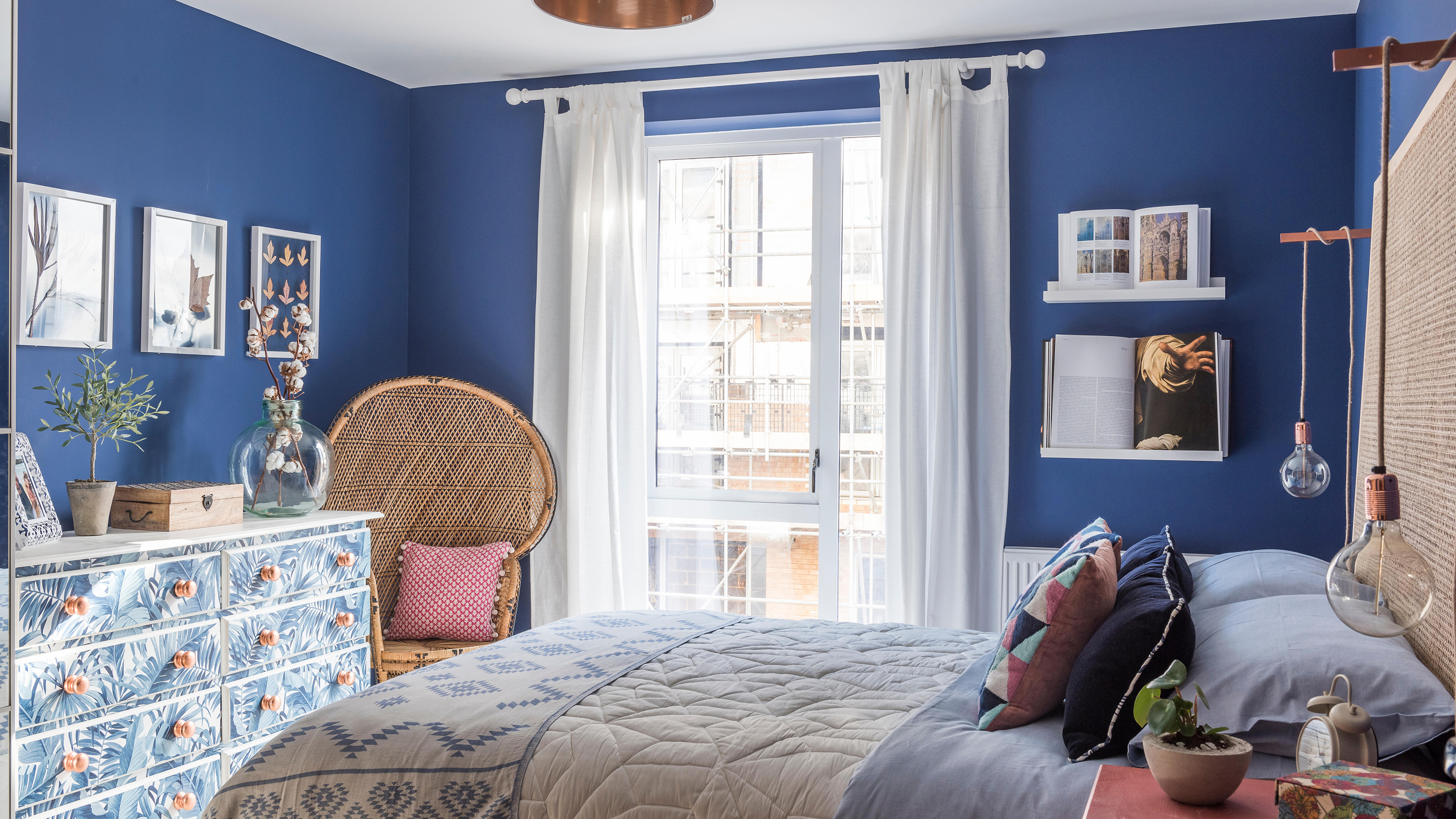 Wicker chair and leaf patterned chest of drawers in blue bedroom of London 
