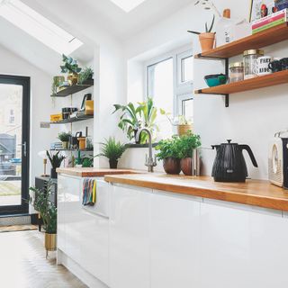 white kitchen with wooden worktops and open shelves beside a UPVC window