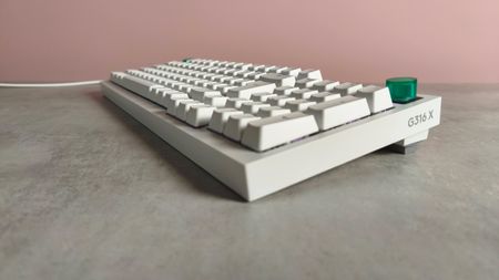 Three-quarter view of Logitech G316 X 98 on a desk with pink wall in background
