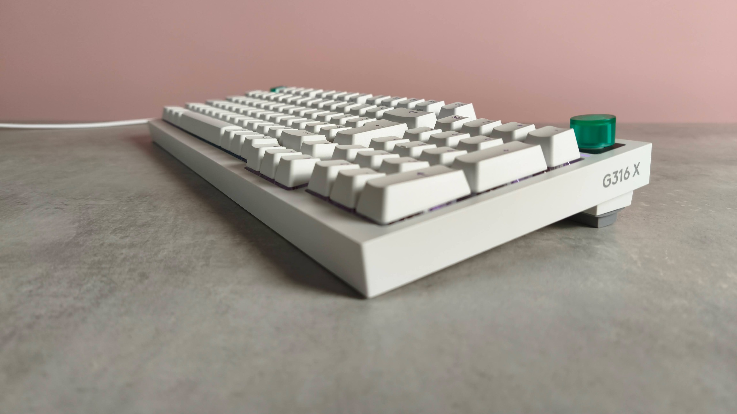 Three-quarter view of Logitech G316 X 98 on a desk with pink wall in background