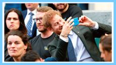 Britain's Prince Harry (R) uses a smartphone to take a photograph as he sits with competitors from the 2014 and 2016 Invictus Games in the crowd