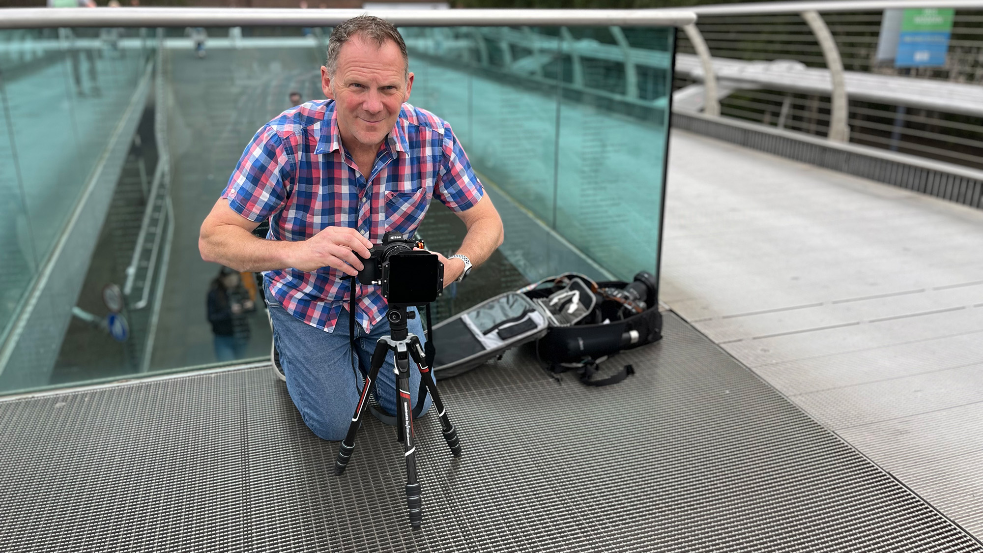 Adam Waring crouching on Millennium Bridge using a camera on a tripod