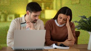 Young couple looking concerned, looking at bills whilst sitting at computer.