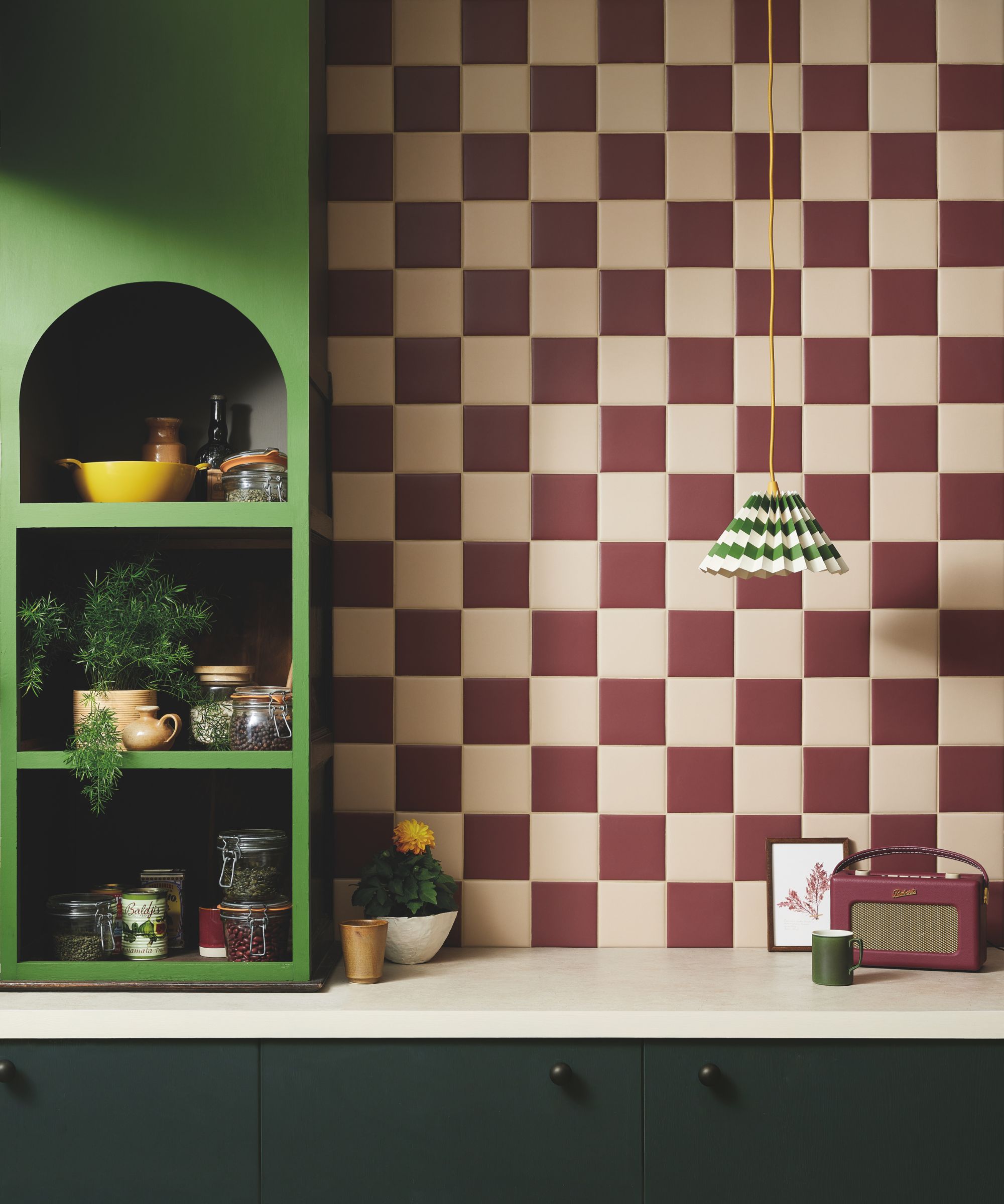 A small kitchen with dark green cabinets, a bold green shelf, and white and merlot checkerboard backsplash tiles