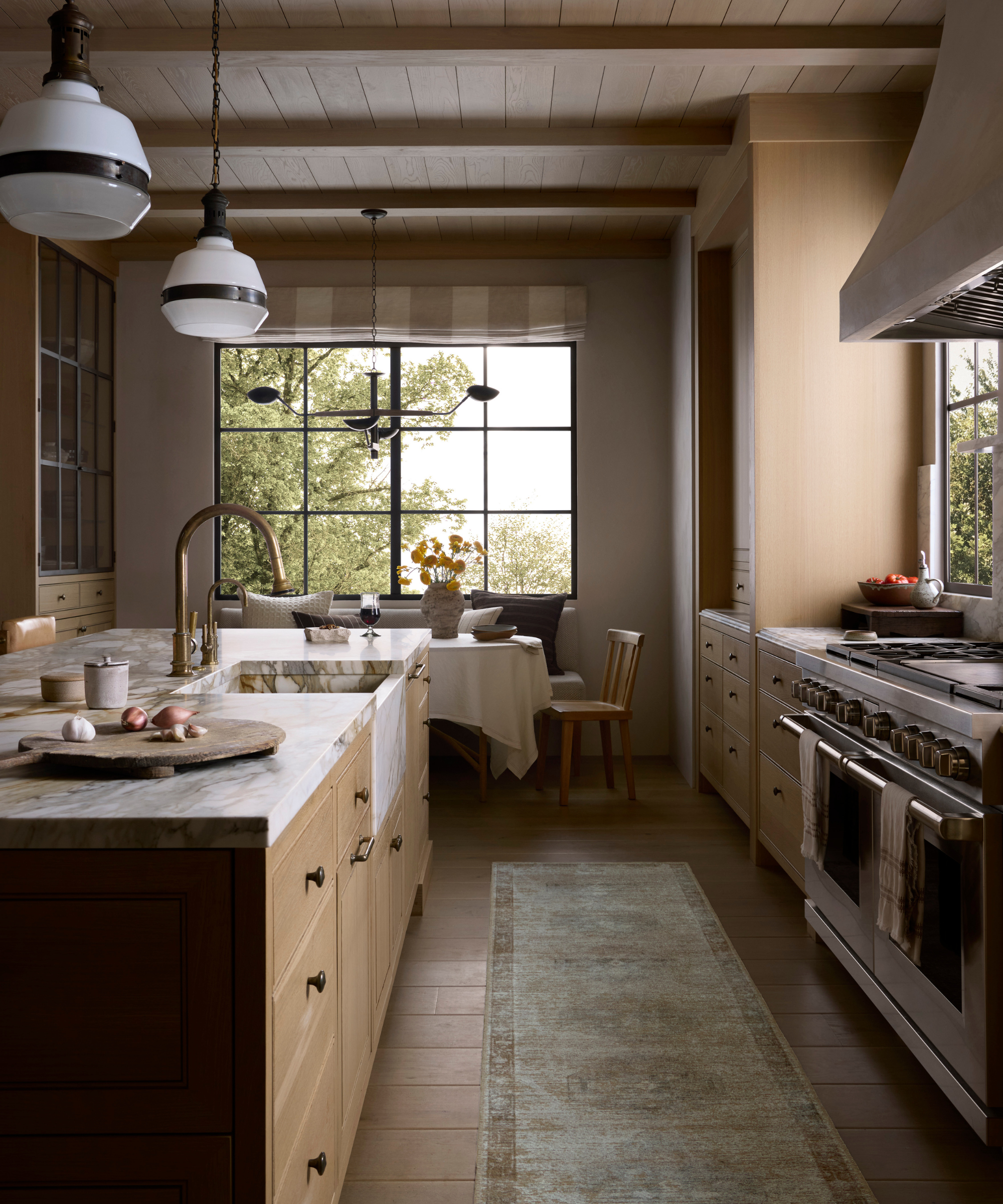a kitchen with a large island with marble countertops, light wood cabinetry, a runner rug, and a large oven