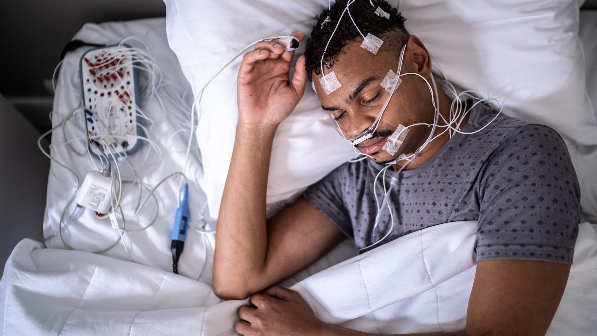 A sleeping person lying in a bed with wires attached to different parts of their head and face.
