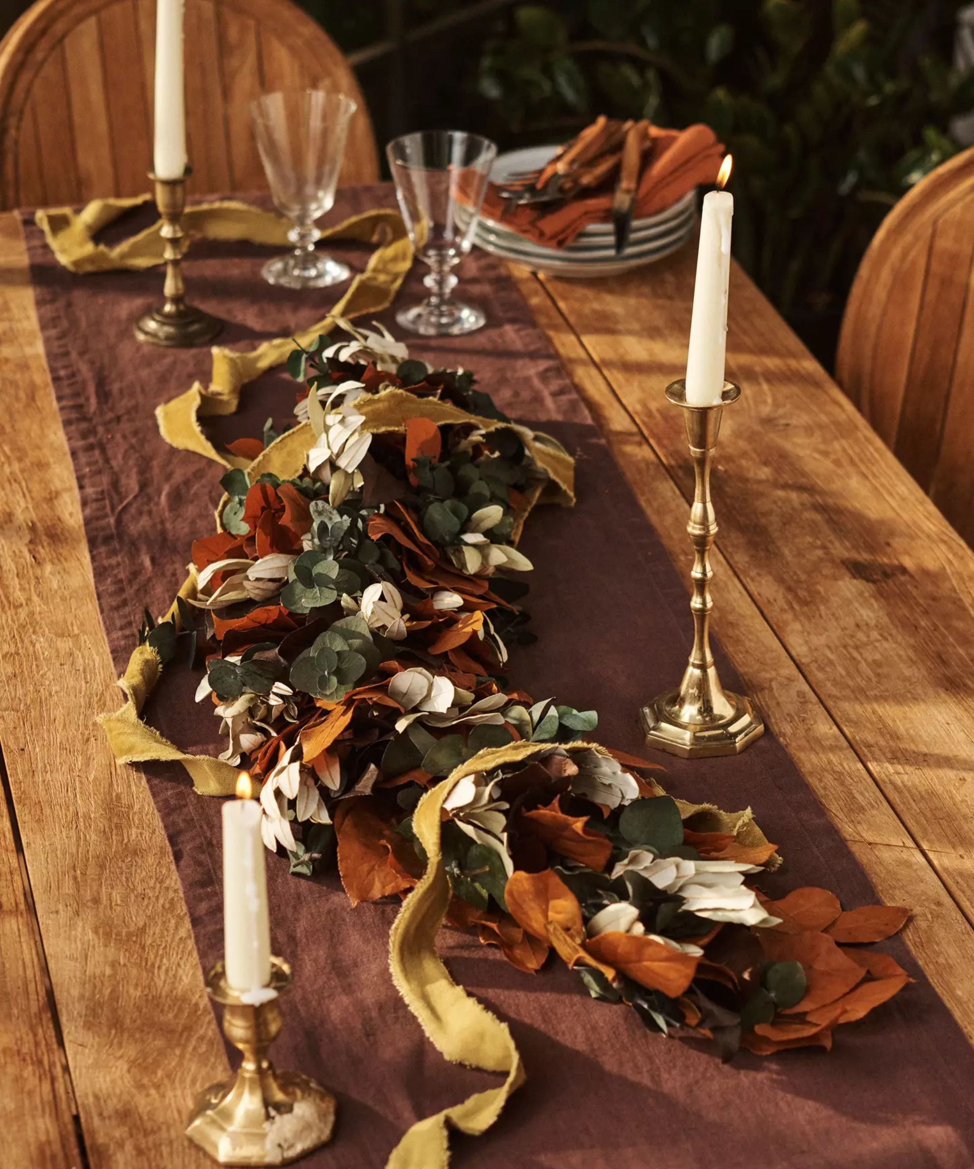Wooden table with brown runnner, fall garland and white taper candles in gold holders