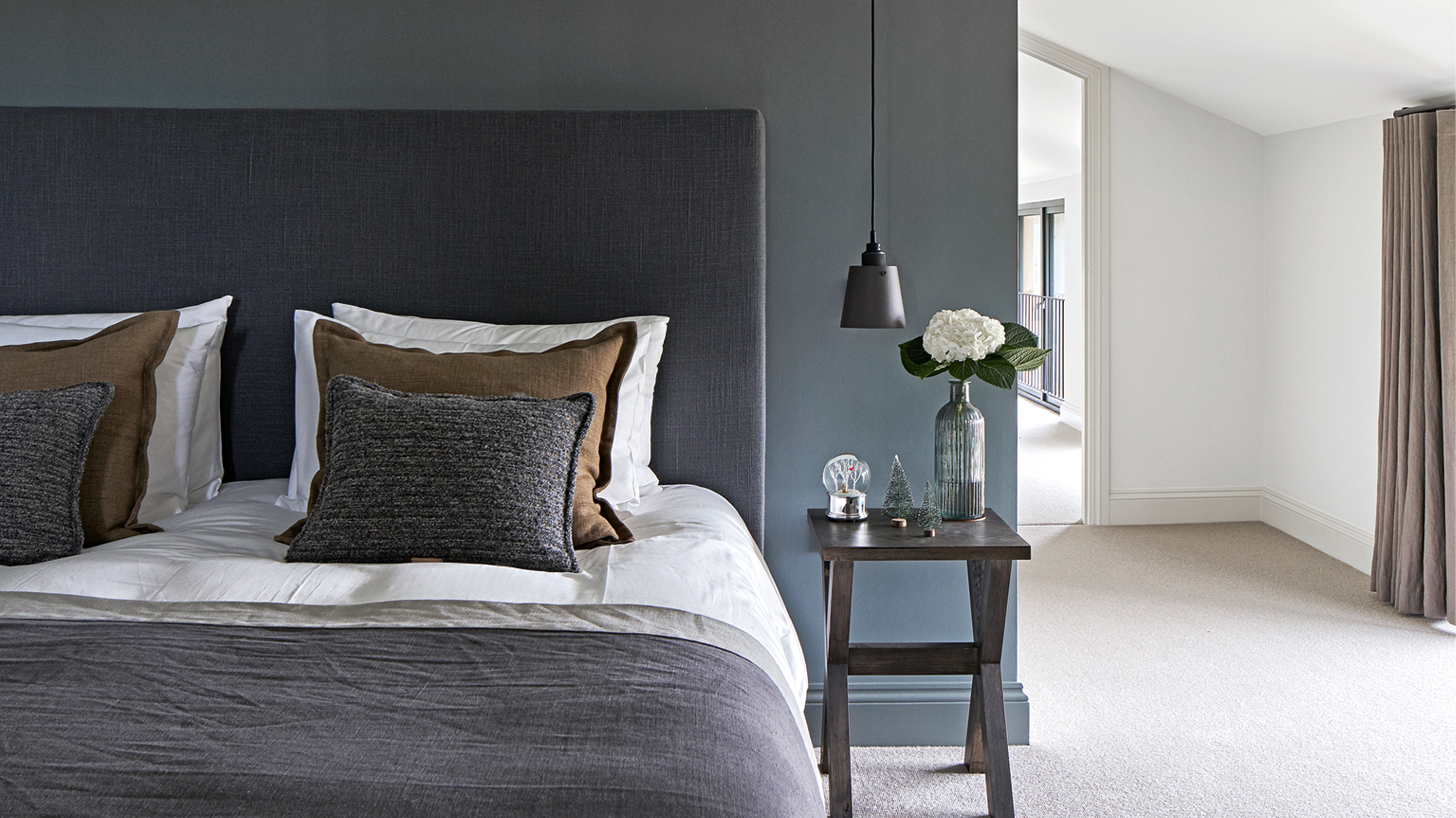 A blue bedroom with a bed dressed in white, grey, and brown bedding