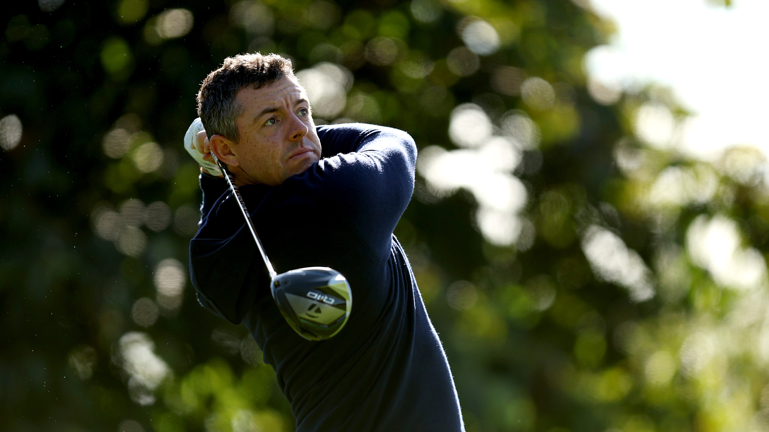 Rory McIlroy holds his finish on a drive wearing a navy hoody and no cap