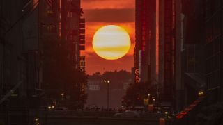 The sun is pictured setting between the high-rise buildings lining New York's 42nd street on July 11, 2023, during the Manhattanhenge season.